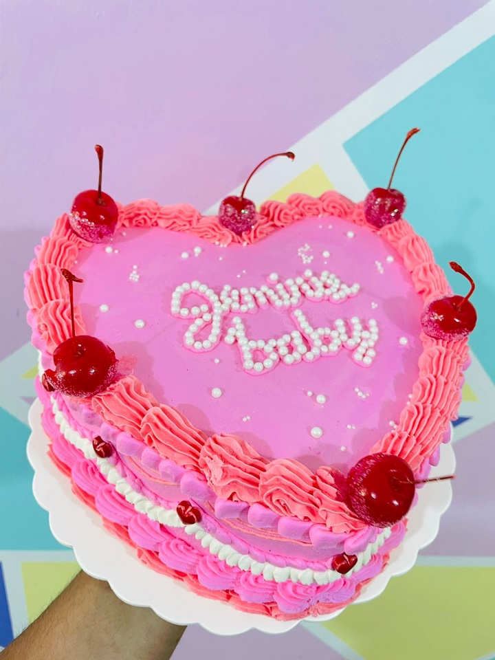 Pastel de baby shower en forma de corazón rosa con cerezas y perlas