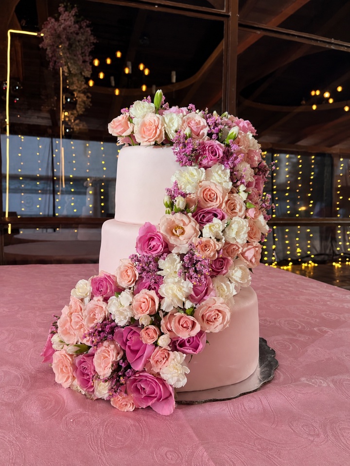 Pastel de boda de tres pisos en rosa con una cascada de flores rosas y blancas