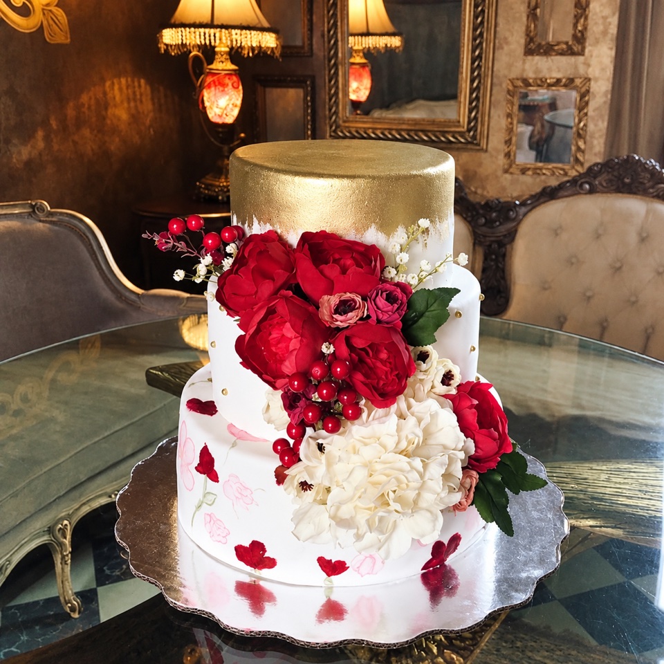 Pastel de boda de dos pisos blanco con tapa dorada y flores rojas y blancas