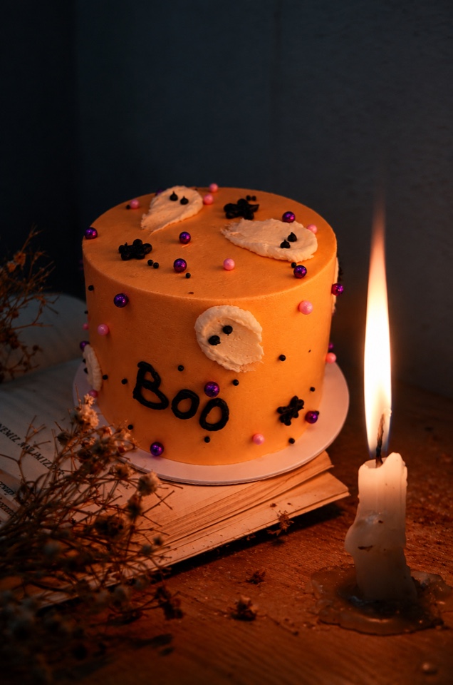 Pastel de naranja decorado de Halloween con letrero BOO, junto a una vela, 10–15 personas