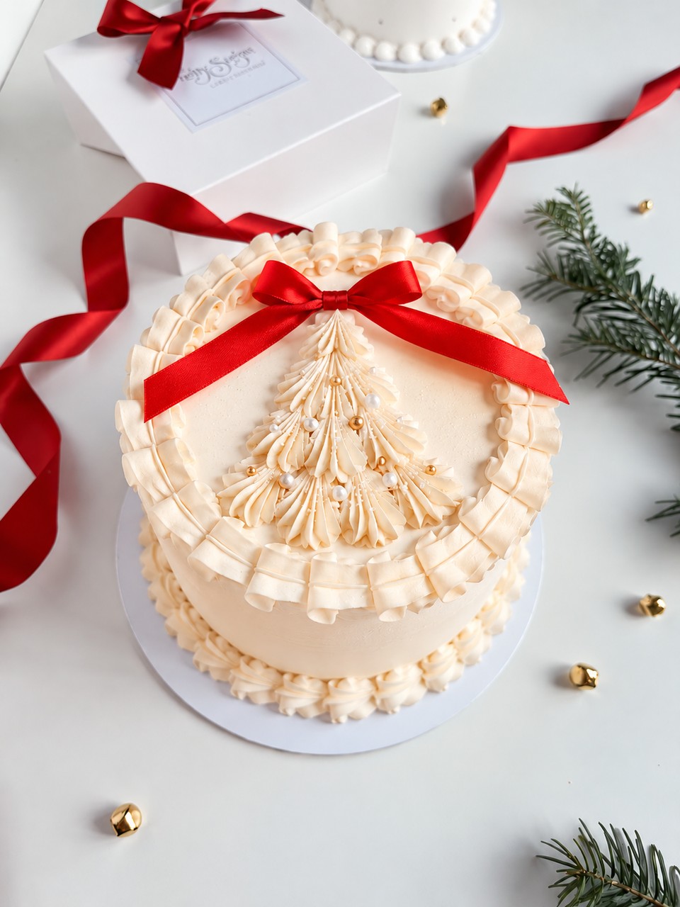 Pastel vainilla clásico navideño, betún crema con arbolito de Navidad y moño rojo, relleno de dulce de leche.